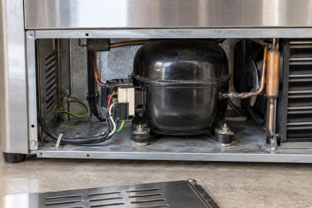 Compressor and start relay exposed behind the lower access panel of an outdoor refrigerator
